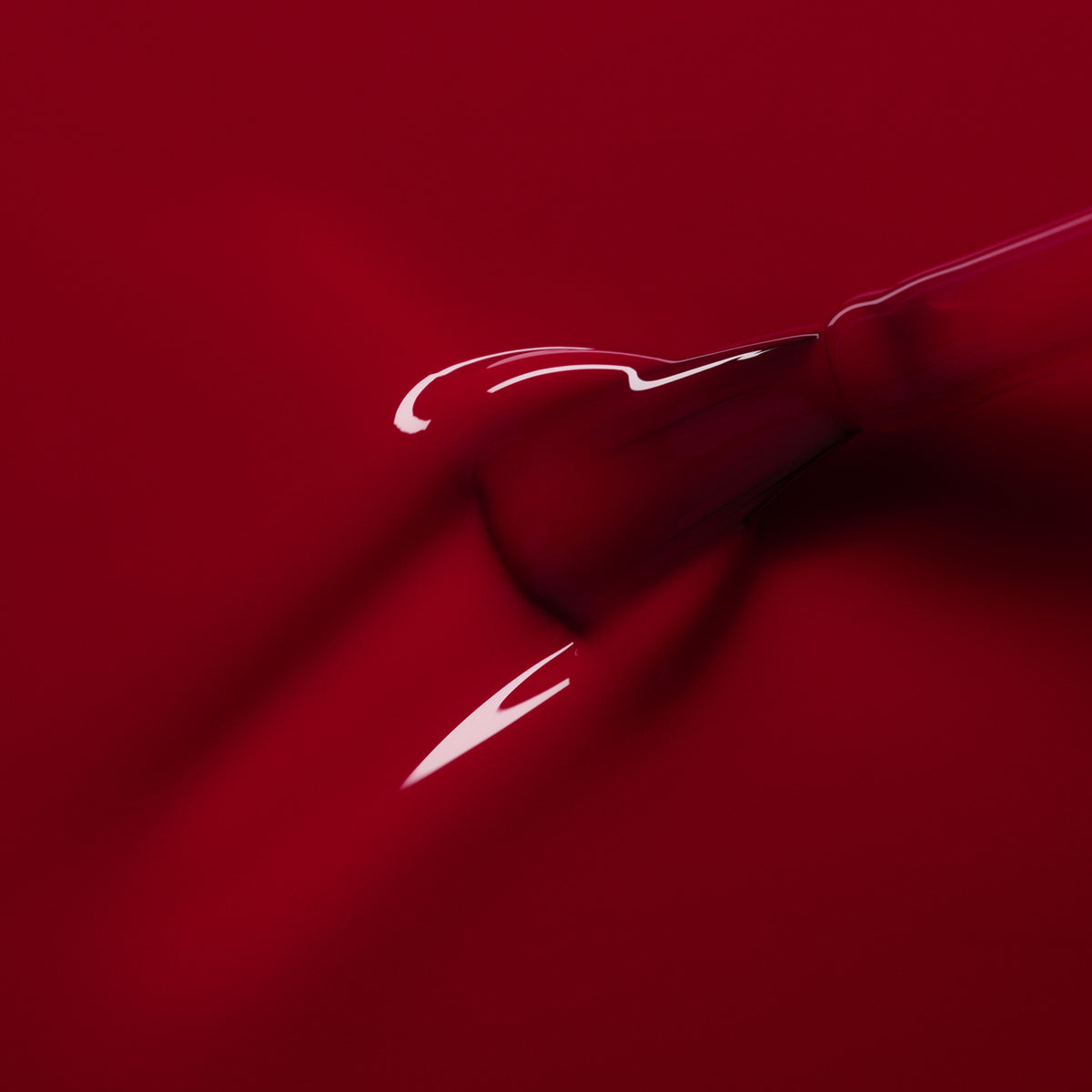 A close-up shows a dropper releasing Manucurist’s Pomegranate gel polish—a glossy raspberry red—onto a smooth red surface, forming a shiny, flowing puddle.