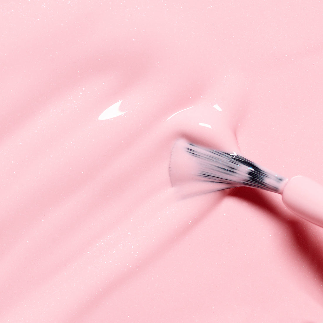 Gros plan d’un pinceau appliquant Rosie the Rabbit de Manucurist, un vernis à ongles rose bonbon pailleté et brillant, créant de douces lignes ondulées sur une surface lisse.