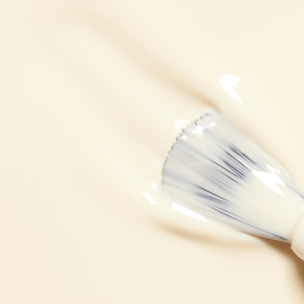 A makeup brush spreads creamy beige foundation over a smooth surface, while hints of Manucurist&