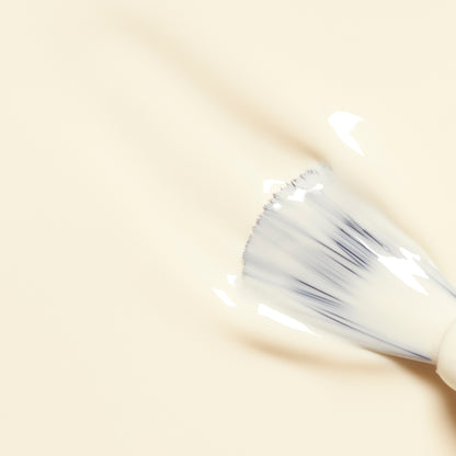 A makeup brush spreads creamy beige foundation over a smooth surface, while hints of Manucurist&