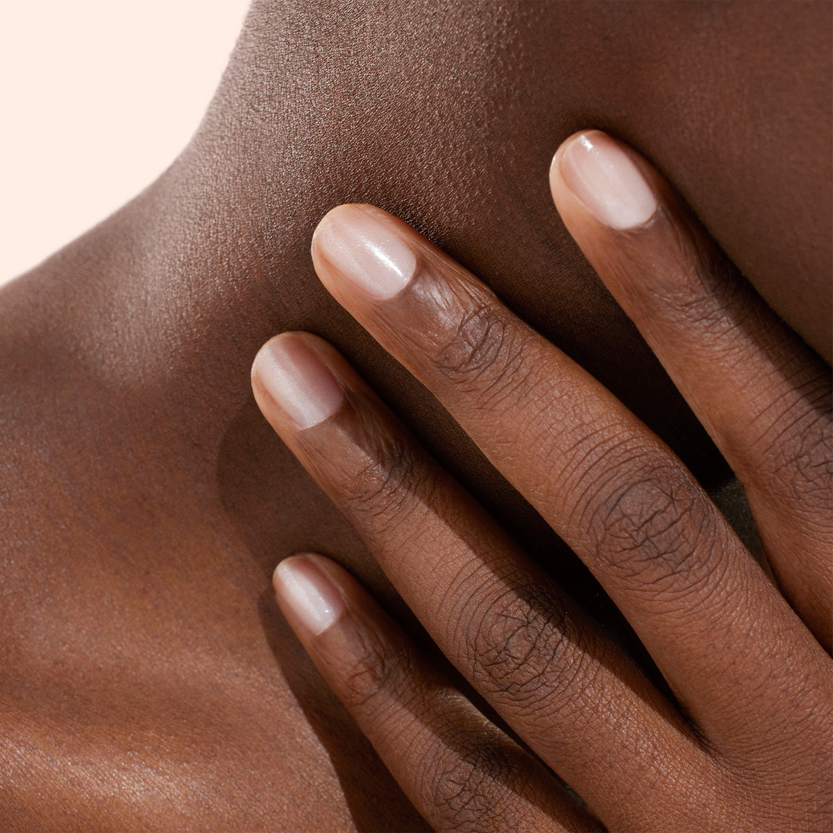 A close-up of a hand with neatly manicured nails, polished with Manucurist’s Active™ Shine Opal plant-based nail polish, gently touching the side of a person’s neck and collarbone against a neutral background.