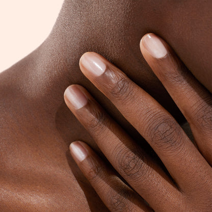 A close-up of a hand with neatly manicured nails, polished with Manucurist’s Active™ Shine Opal plant-based nail polish, gently touching the side of a person’s neck and collarbone against a neutral background.