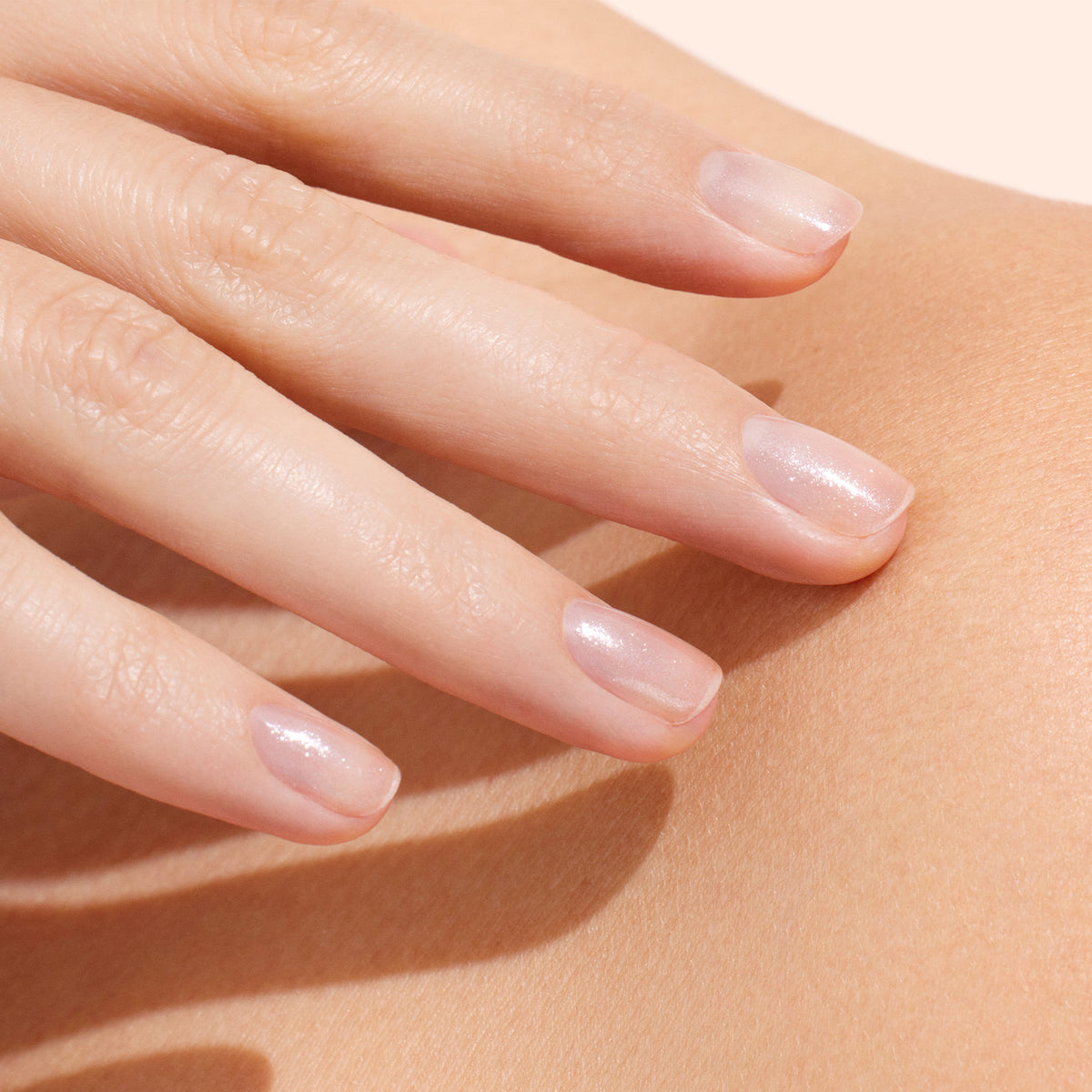 A close-up of a hand with natural, glossy, light pink nails—enhanced by Manucurist’s Active™ Shine Opal plant-based nail polish—gently resting on smooth, bare skin.