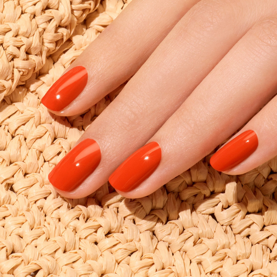 Une main aux ongles soigneusement manucurés, vernis avec la teinte Coral Reef de la gamme Green™ de Manucurist, repose sur une surface beige tissée et texturée.