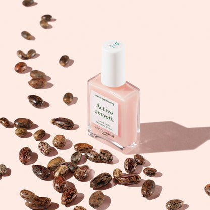 A bottle of Manucurist Active™ Smooth 00 pink nail polish sits on a light pink surface, surrounded by scattered brown seeds and casting a soft shadow—ideal for anyone seeking plant-based nails or an advanced nail treatment.