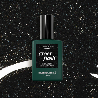 Un flacon de vernis semi-permanent Manucurist Sparks posé à la verticale sur un fond noir parsemé de mouchetures blanches semblables à des étoiles.