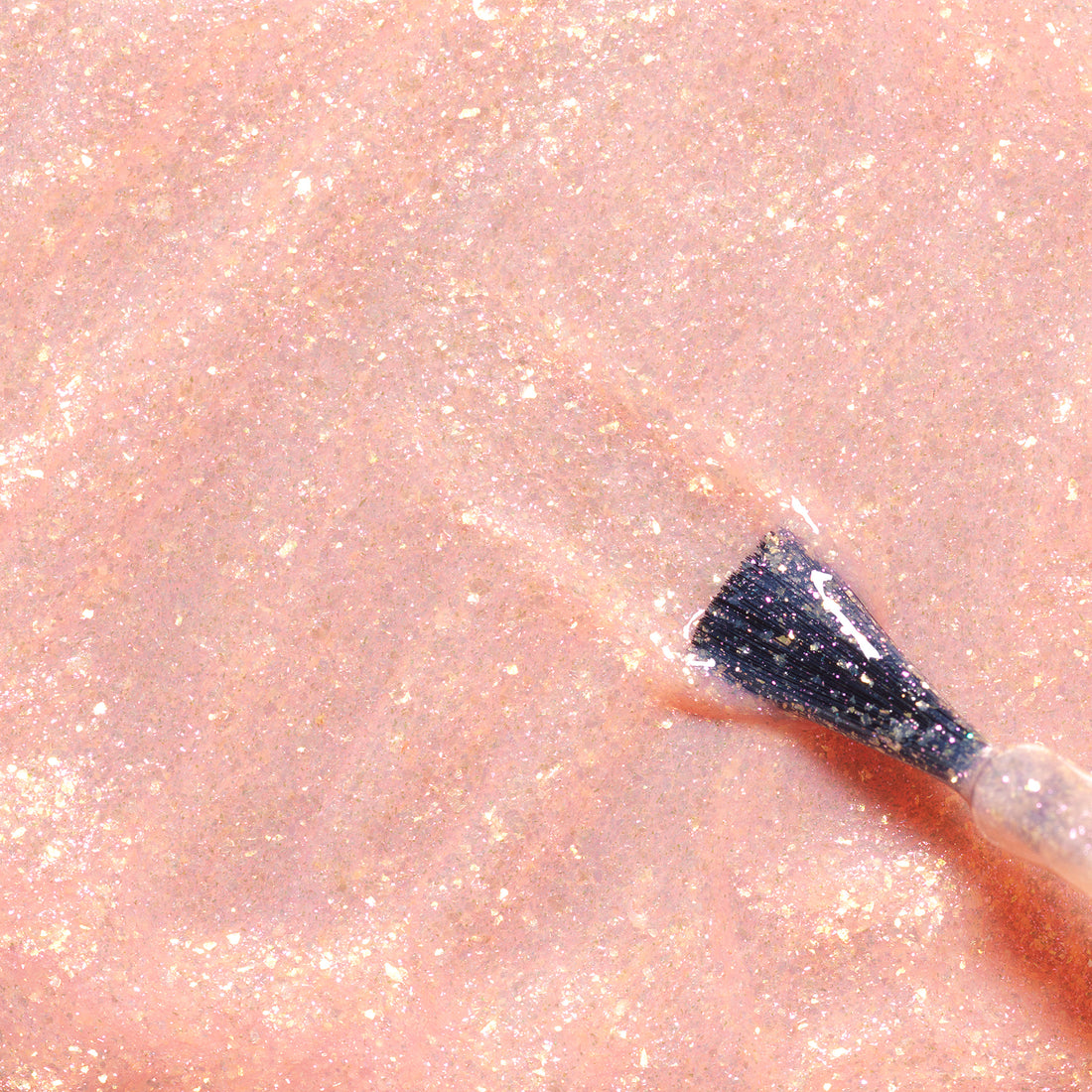 Gros plan d’un pinceau de vernis à ongles appliquant Stella the Starfish de Manucurist, un vernis à ongles rose pâle scintillant pour enfants aux paillettes dorées, formulé à partir d’ingrédients d’origine naturelle, sur une surface lisse.