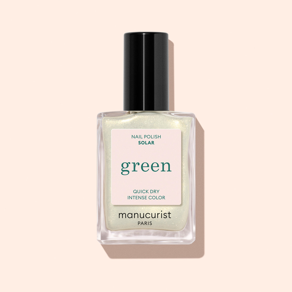 A bottle of Manucurist Solar nail polish in a shimmery pale shade with golden shimmer, black cap, and label reading "Nail Polish Solar, Quick Dry Intense Color" on a light pink background.