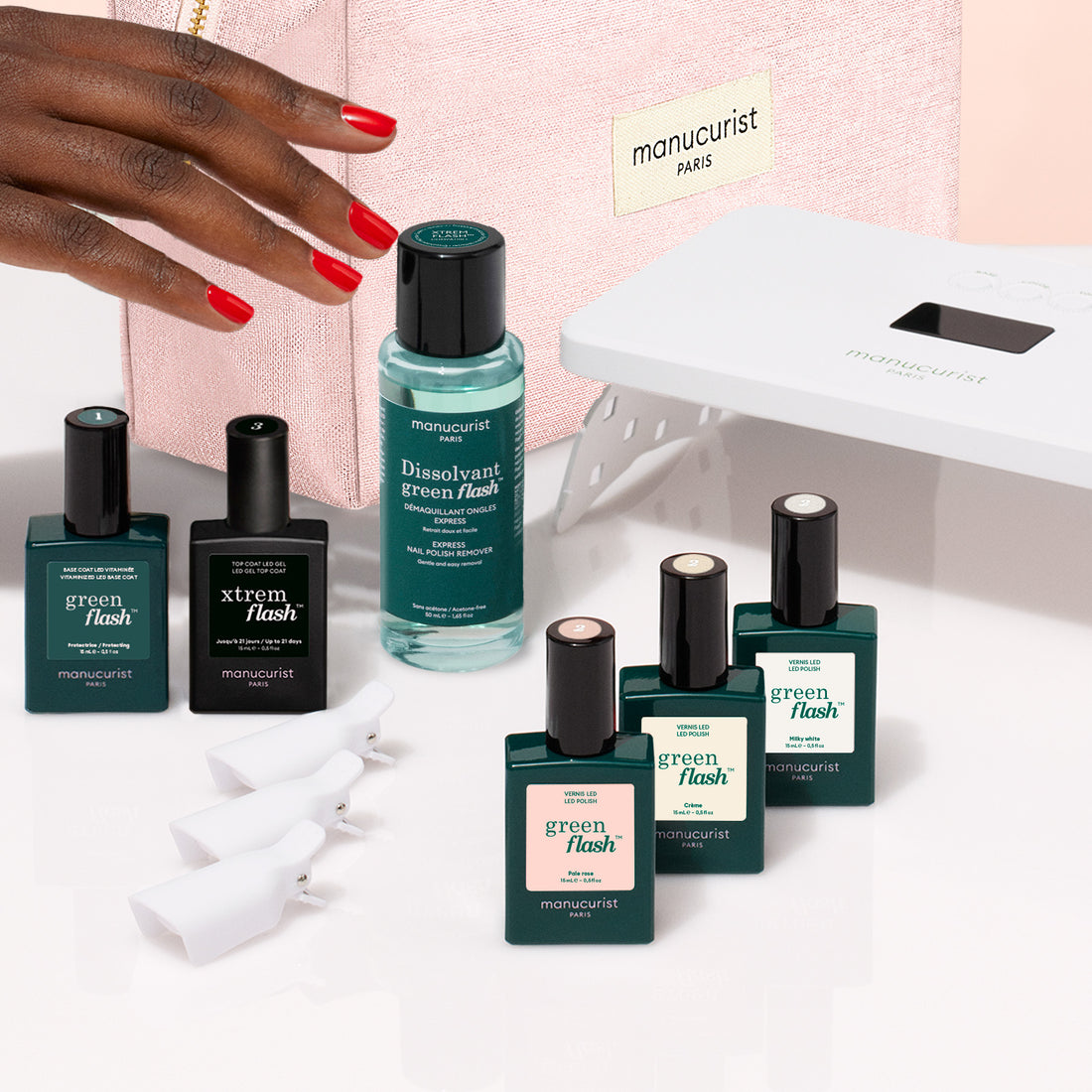 Une main aux ongles vernis de rouge à côté d’un Starter Kit de vernis semi-permanent LED Soap Nails, avec un flacon de dissolvant, quatre pinces à ongles blanches et une lampe LED portable pour une manucure ultra-brillante.