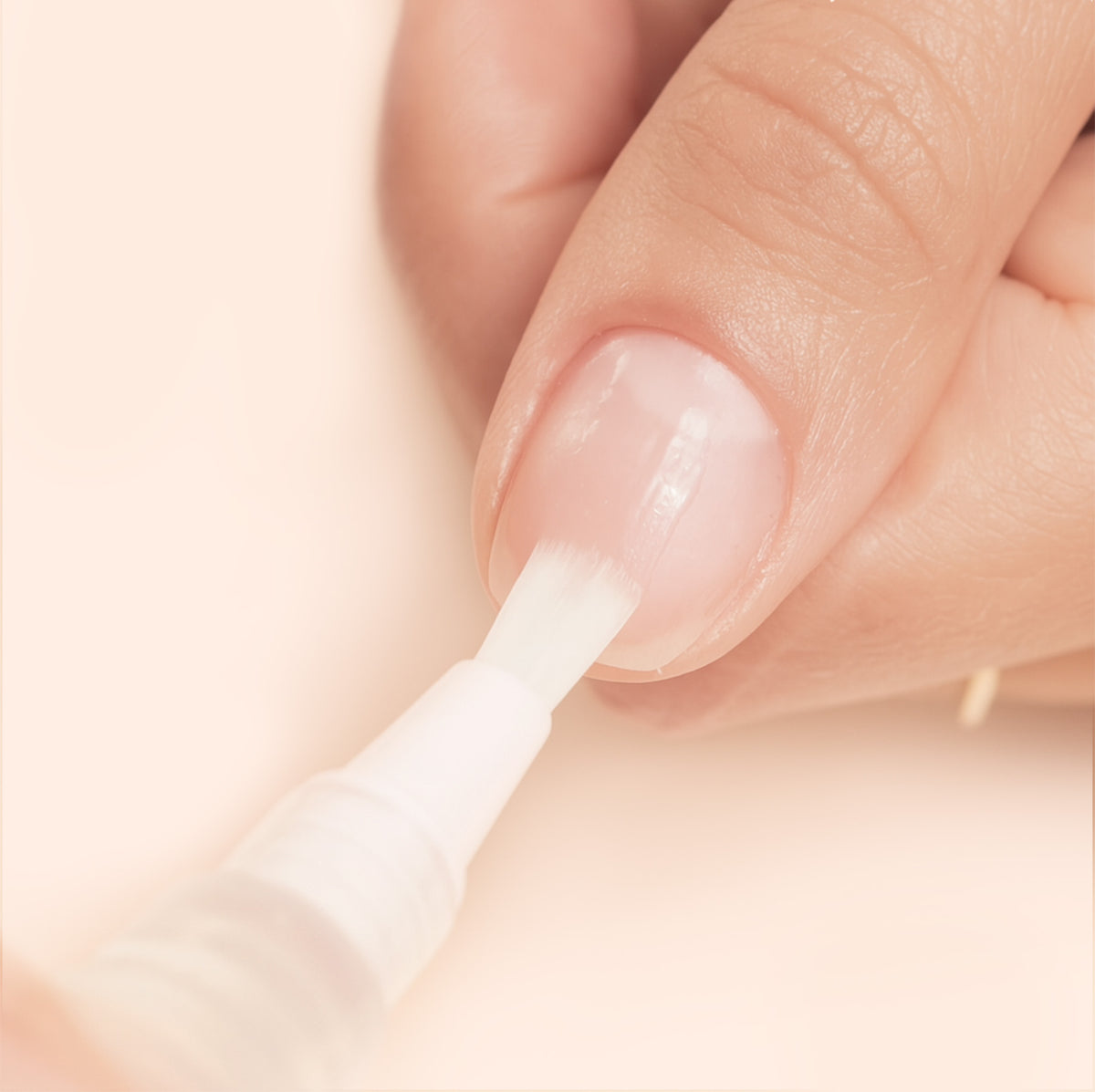 A close-up of a hand applying clear nail polish to a fingernail with a brush applicator, showing well-groomed nails and smooth skin.