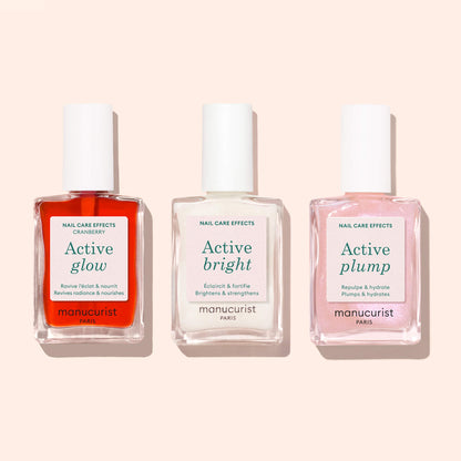 Three bottles of Manucurist nail care treatments—Active™ Glow Cranberry (red), Active Bright (white), and Active Plump (pink)—are displayed side by side on a light beige background, highlighting the brand’s dedication to plant-based nail care and radiant, beautifully tinted nails.