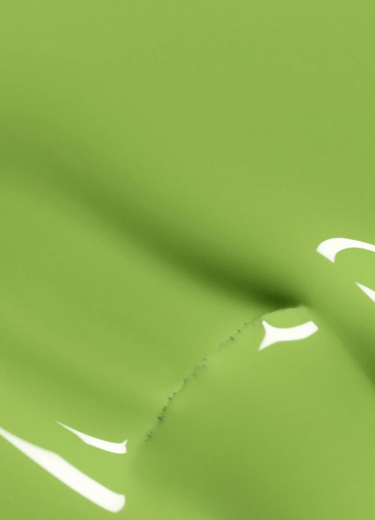 A close-up of bright green fabric with a visible seam and partial white printed design, possibly a number or letter, creating a soft and slightly abstract appearance.