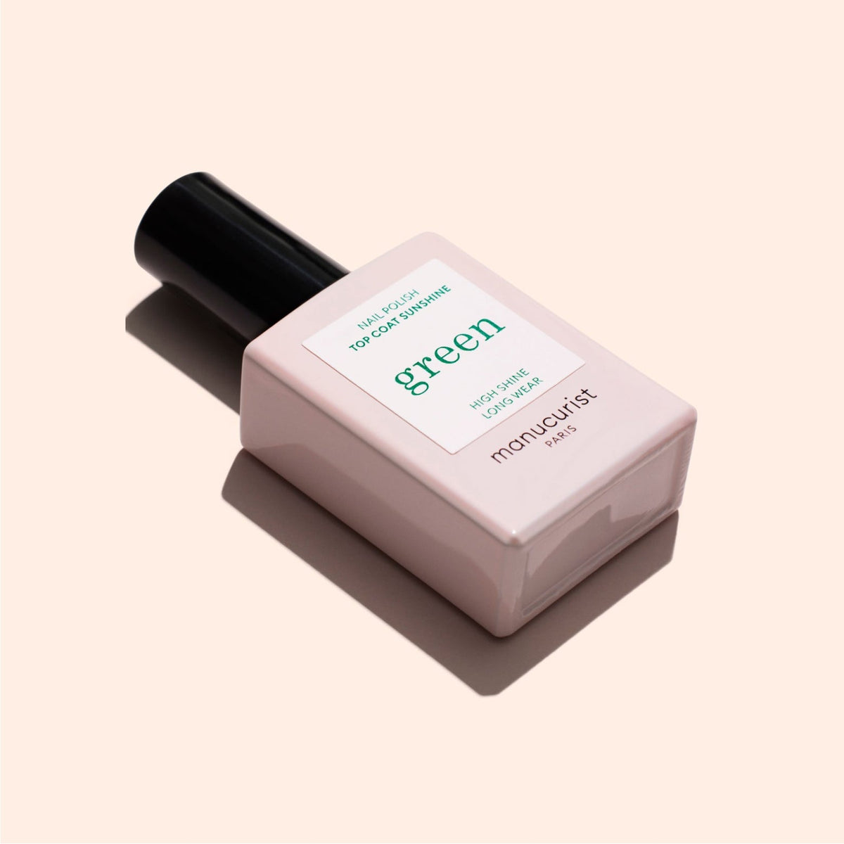 A rectangular, pale pink bottle of Manucurist Paris nail polish with a black cap, labeled Green and featuring minimalist design, is shown on a light beige background.