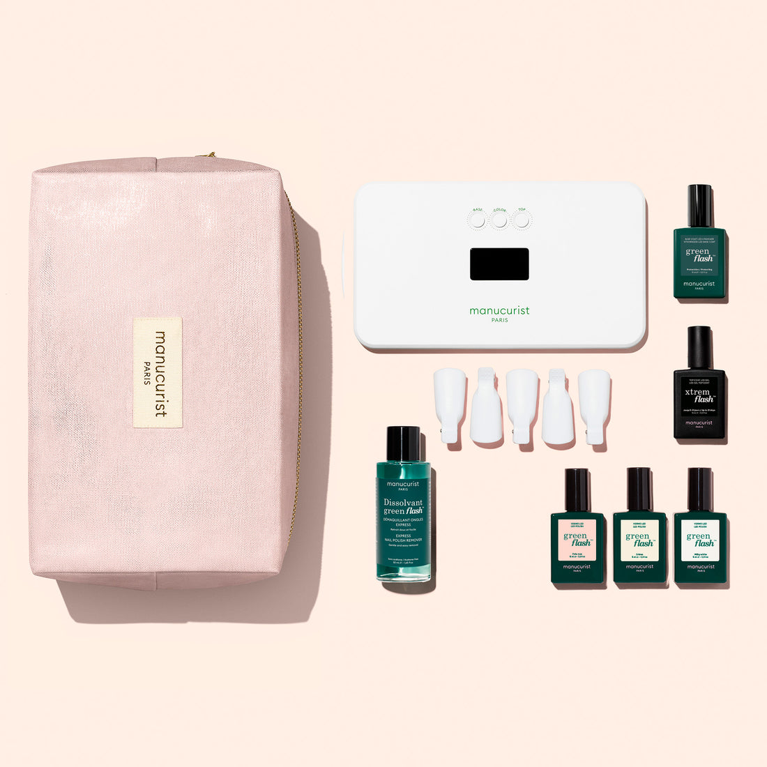 Un Starter Kit Manucurist de vernis semi-permanent LED Soap Nails, comprenant une lampe LED blanche, du dissolvant, cinq vernis colorés, un Top Coat et cinq pinces pour les doigts, disposés à côté d’une trousse de maquillage zippée.