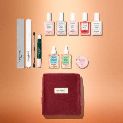 The Manucurist Active™ Super Ultimate Gift Set is perfect for your active manicure routine, featuring files, a cuticle tool, nail polishes, gentle nail remover, cuticle oils, balm, and a red velvet pouch—all arranged neatly on a peach-colored background. Ideal as a thoughtful holiday gift.