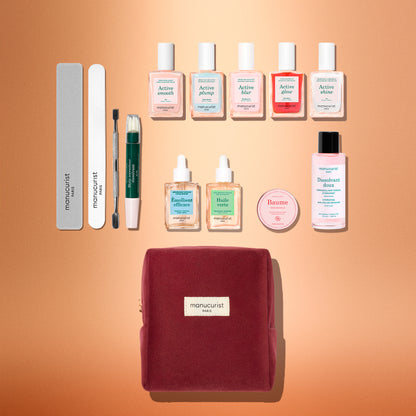 Introducing the Manucurist Active™ Super Ultimate Gift Set: a meticulously arranged collection featuring nail files, a cuticle care tool, eight nourishing nail care bottles, a gentle nail remover bottle, a pink balm tin, and an elegant burgundy velvet pouch—all displayed on a peach background. Perfect for enhancing your active manicure routine or gifting as an extra-special holiday treat.