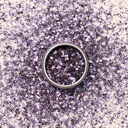 A silver ring sits on a surface dusted with Manucurist’s Lilac Biodegradable Glitter, creating a sparkling, colorful backdrop ideal for nail art inspiration.