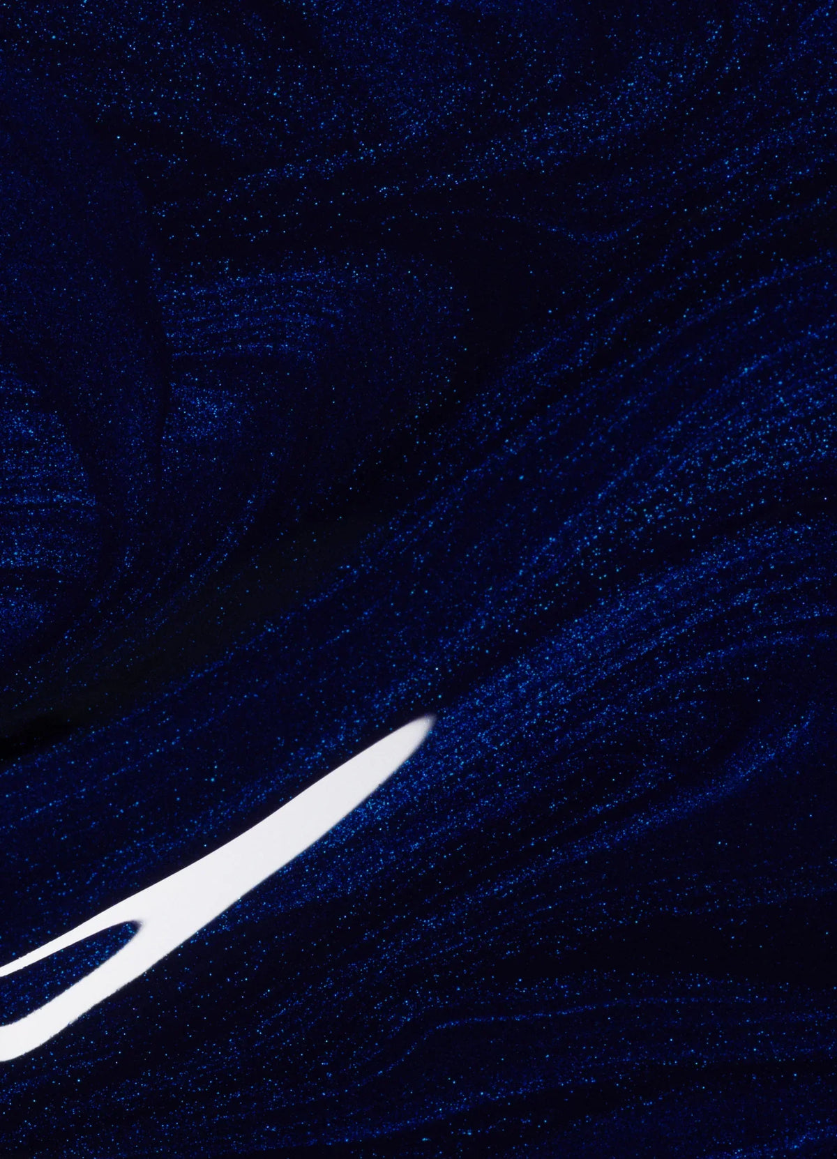 An abstract image featuring swirling, glittery dark blue patterns with a bright white, pointed streak cutting through the lower left area.