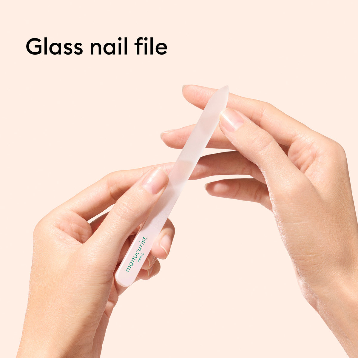Une personne façonne ses ongles avec un trio d’accessoires pour ongles en verre Manucurist-us, comprenant une lime en verre transparente, tandis que "Lime à ongles en verre" apparaît en haut à gauche sur un fond clair. Un repousse-cuticules en verre complète la routine de manucure.