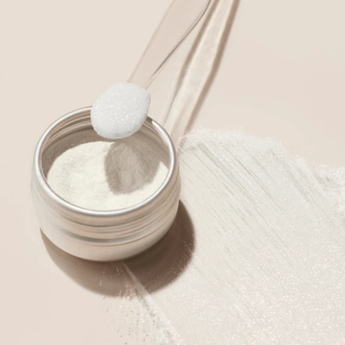 A small jar of Manucurist White Glazed Effect Powder sits open on a light surface, with a clear spoon holding a scoop above it and a streak of powder beside—ideal for creating stunning white glazed nails in your next manicure.