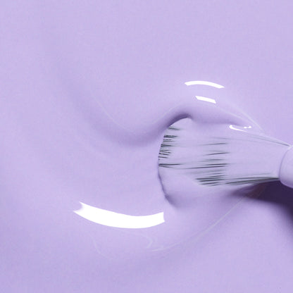 Gros plan sur un pinceau faisant tournoyer Wisteria de Manucurist, un vernis gel violet pastel lisse et brillant, créant de délicates stries courbes à la surface.