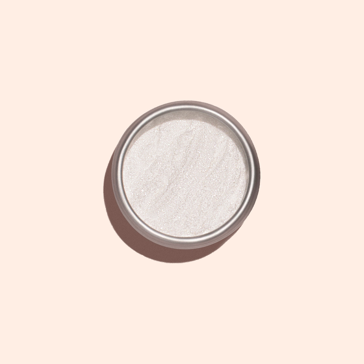 La poudre White Glazed Effect Powder de Manucurist, une poudre blanche scintillante très fine dans un petit boîtier métallique rond, est présentée sur un fond beige clair avec une ombre douce sur la gauche — idéale pour créer des looks glazed.