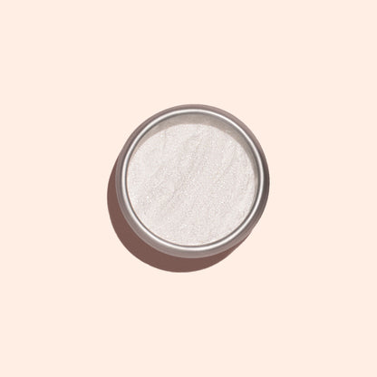 La poudre White Glazed Effect Powder de Manucurist, une poudre blanche scintillante très fine dans un petit boîtier métallique rond, est présentée sur un fond beige clair avec une ombre douce sur la gauche — idéale pour créer des looks glazed.