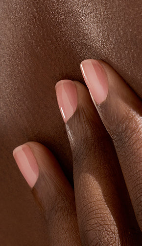 A close-up of a hand with neatly manicured, pale pink nails gently resting on dark, smooth skin.