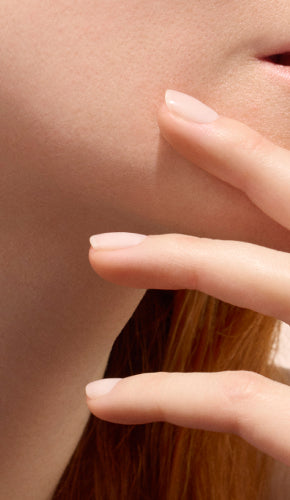 A close-up of a person’s lower face and chin with two fingers gently touching the skin. The nails are neatly manicured with a light, natural polish. The image highlights smooth, healthy skin and well-groomed nails.