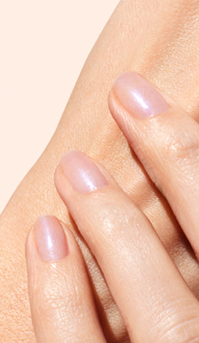 A close-up of a hand with three fingers gently touching the skin of another part of the hand, displaying short, neatly manicured nails with a light, natural pink polish.