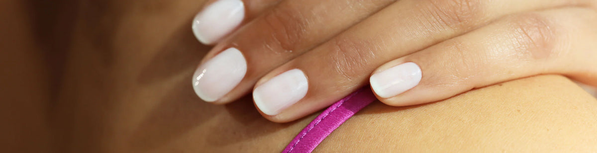 A close-up of a hand with neatly manicured white nails resting on skin near a pink strap.