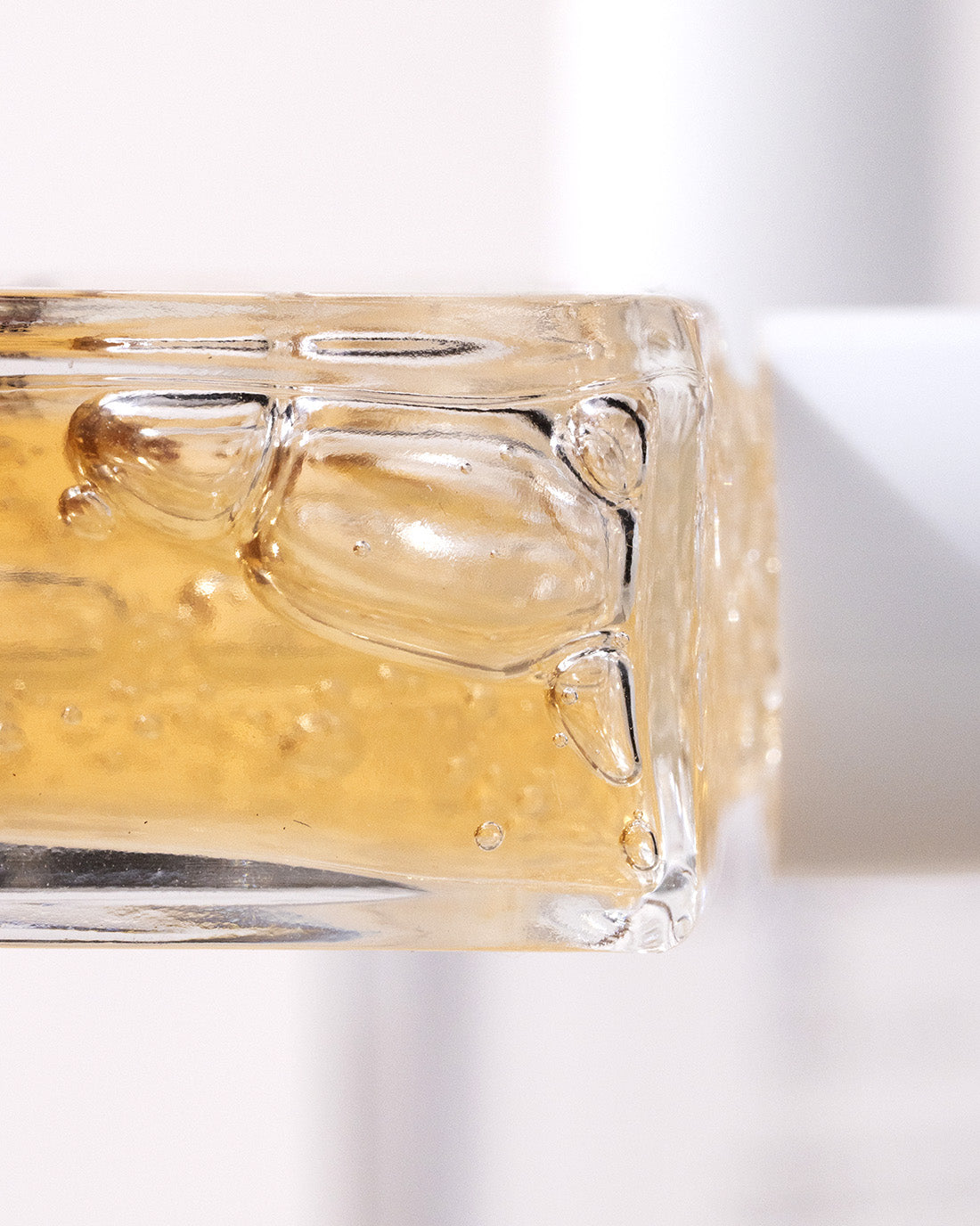 Close-up of a glass container filled with thick, golden liquid and air bubbles, possibly honey or gel, against a light, blurred background.