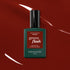 A bottle of Manucurist Bohème Green Flash LED polish—a Montmartre-inspired red-brown shade—rests on a glossy deep red surface with light reflections. The dark green bottle features a black cap and a red label.
