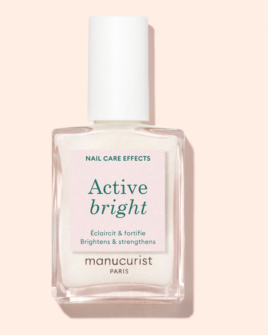 A bottle of Manucurist Paris nail care polish labeled Active Bright with text indicating it brightens and strengthens nails. The bottle sits on a light pink background.