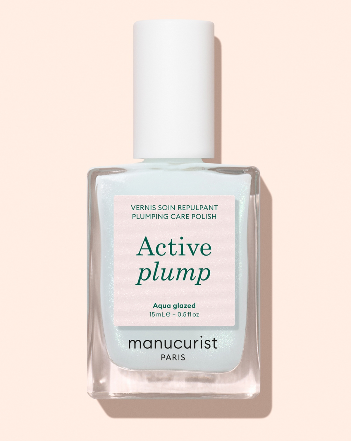 A clear bottle of polish labeled Active plump by Manucurist Paris, with a white cap and aqua-glazed text, set against a light peach background.