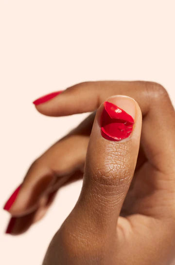 A close-up of a hand with red nail polish, showing a partially peeled-off layer of polish on the thumb. The background is a plain, light color.
