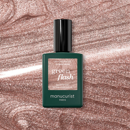Un flacon de vernis à ongles Manucurist Cosmic Rose est posé sur un fond rose scintillant qui complète parfaitement cette teinte rose irisée.