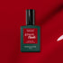 A bottle of Manucurist Dark Dahlia gel polish sits on a red background. The green bottle with a black cap and red label showcases the rich hue of the Dark Dahlia shade.