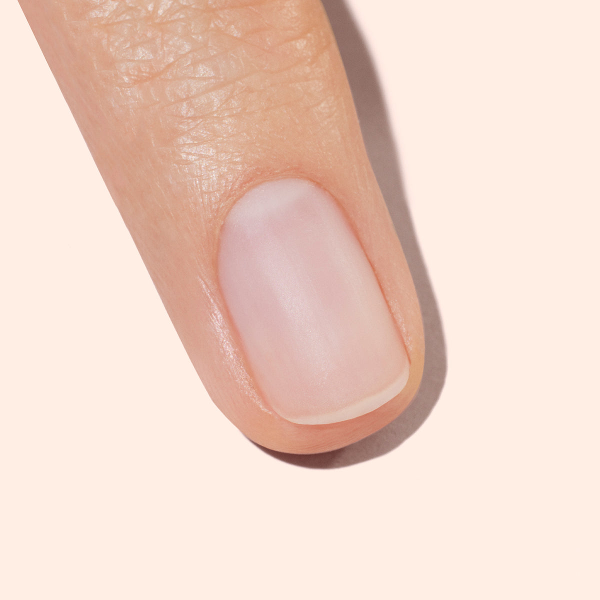 A close-up of a fingertip showing a clean, well-groomed natural fingernail against a light, neutral background.