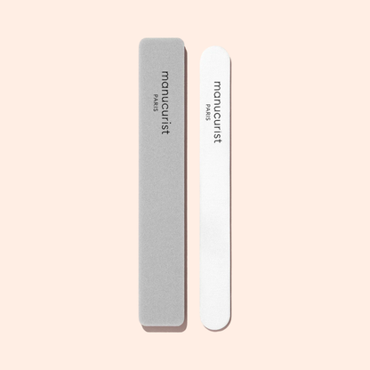 A Manucurist Nail Buffer Sponge with rounded edges sits next to a gray nail file, both ready to smooth your nails on a light beige background.