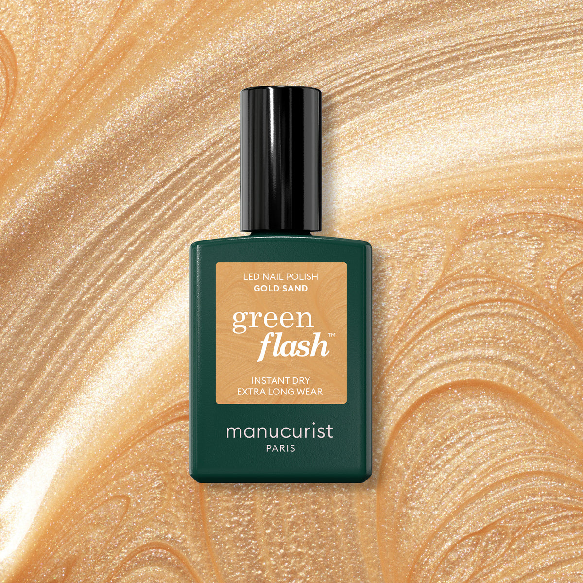 A bottle of Manucurist’s Gold Sand gel nail polish rests on a gold sand background, its label featuring instant dry and extra long wear benefits with an iridescent shine.