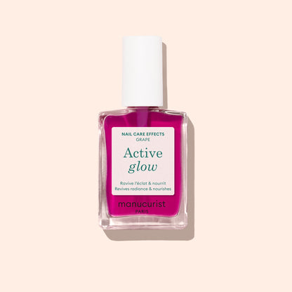 Un flacon de soin pour les ongles Active™ Glow Grape de Manucurist, avec un bouchon blanc et un liquide rose, conçu pour sublimer votre brillance naturelle, présenté sur un fond beige clair.