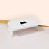 La lampe Premium 36W Manucurist Green Flash™ — une lampe LED blanche rectangulaire avec écran numérique et boutons de commande — est posée sur une surface rose clair et en bois, idéale pour sécher rapidement le vernis gel Green Flash™.
