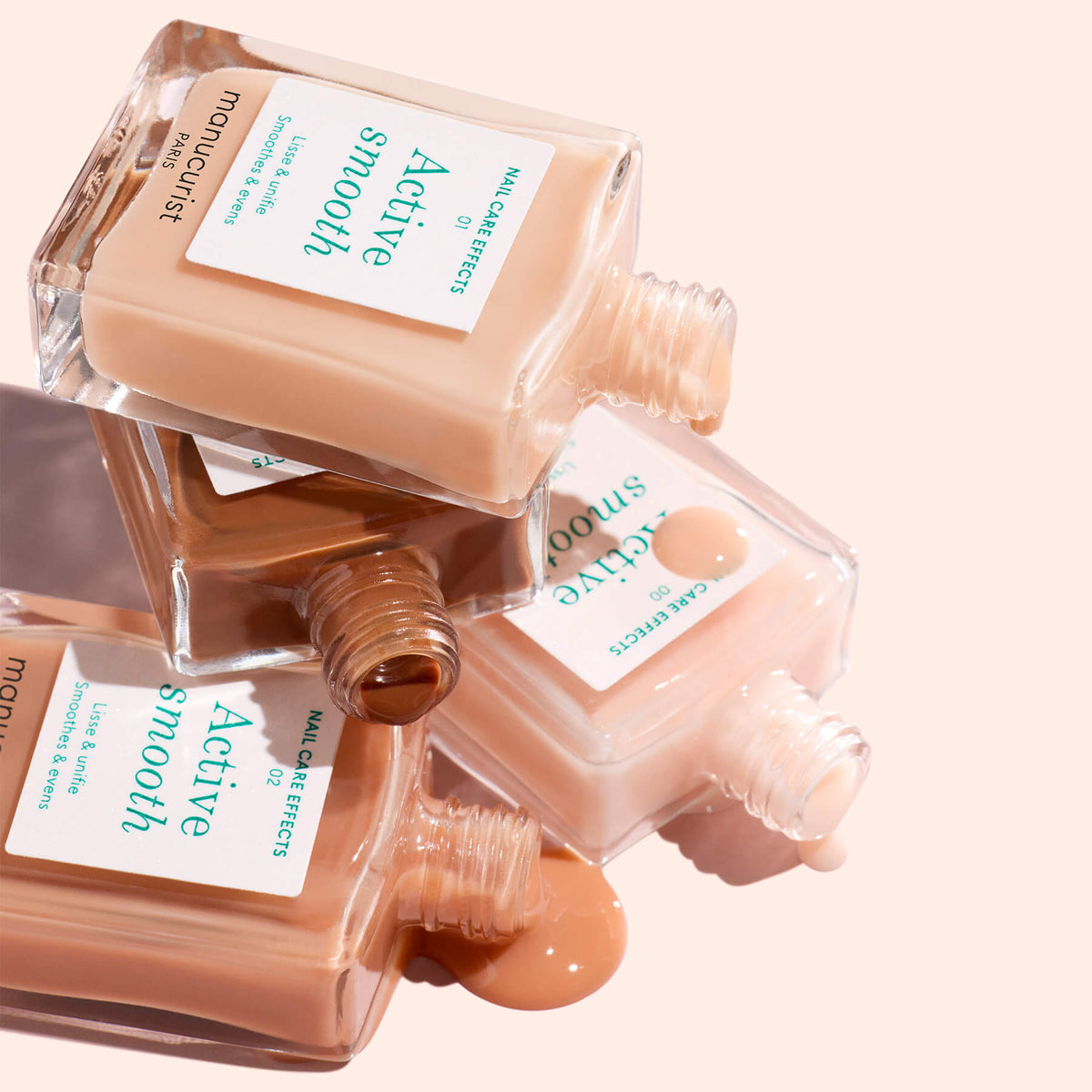 Three bottles from the Manucurist Customizable Active 5-pack are stacked and tipped over, with beige, light tan, and medium brown shades spilling onto a pale pink surface for stunning nail effects and a personalized look.