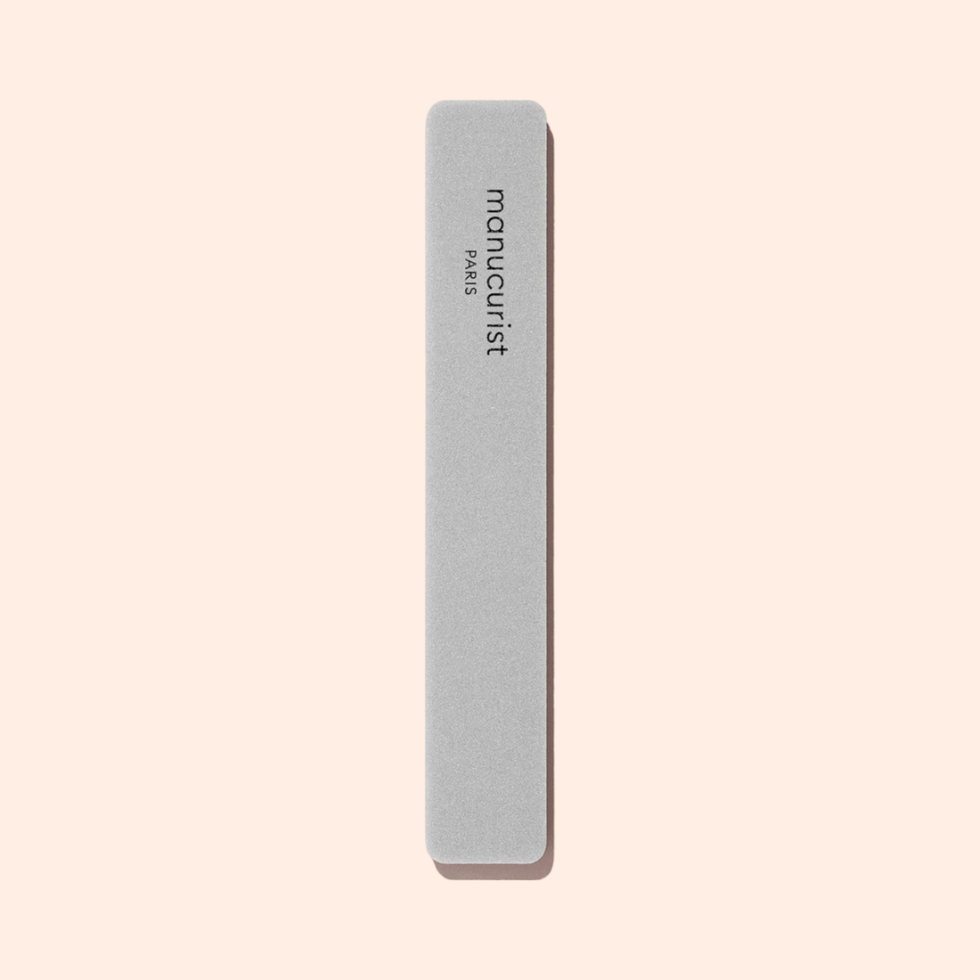 A rectangular gray Manucurist Nail buffer sponge with rounded edges is placed vertically on a light beige background, perfect for smoothing the nail plate and prepping your manicure.