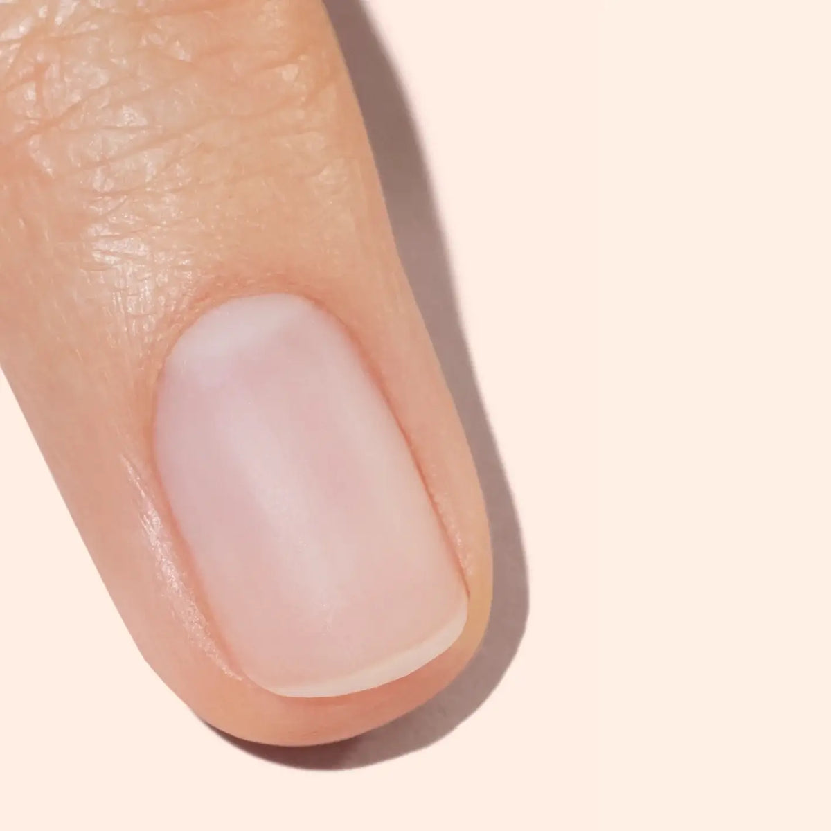 Gros plan d’un ongle et du bout du doigt propres et soigneusement coupés d’une personne, sur un fond beige clair.