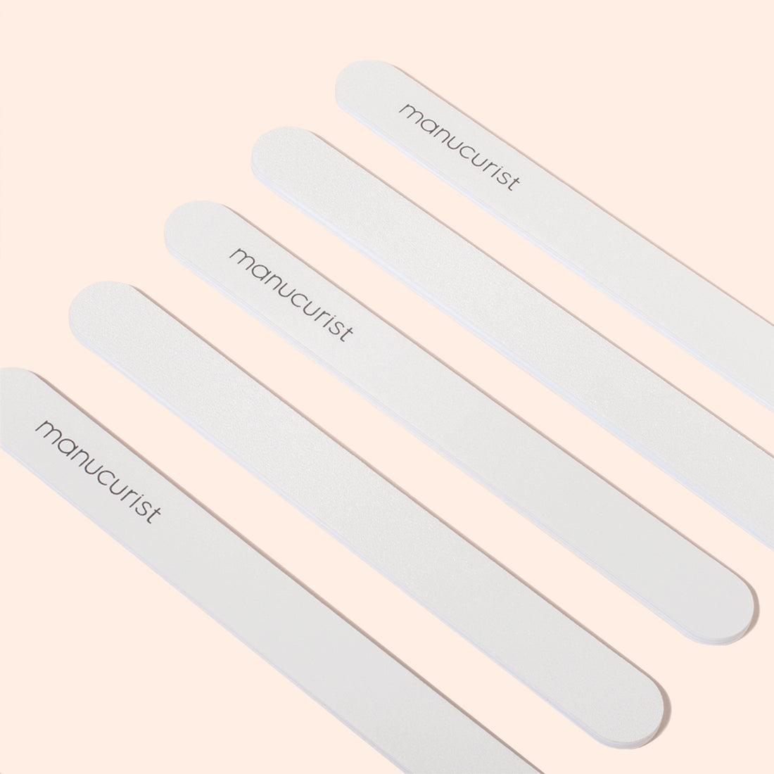 Five Manucurist Emery boards are arranged diagonally on a light beige background. Each file, featuring a fine grit surface, displays the brand name Manucurist printed in black letters.
