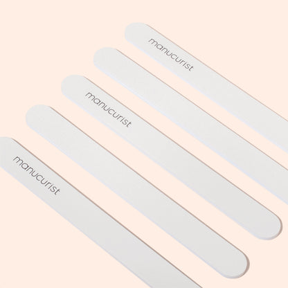 Five Manucurist Emery boards are arranged diagonally on a light beige background. Each file, featuring a fine grit surface, displays the brand name Manucurist printed in black letters.