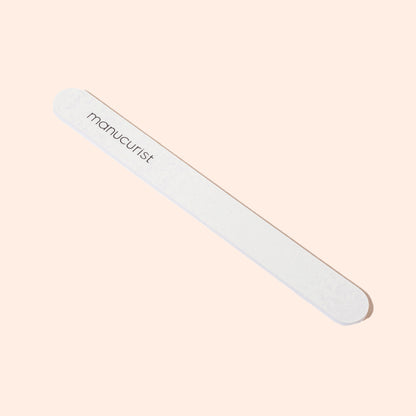 The Manucurist-us 1 Nail File, a white 100/180 grit emery board with rounded edges and "manucurist" printed on it, is ideal for shaping natural nails and is shown on a light beige background.