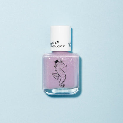 Un flacon de vernis à ongles pour enfants Manucurist Janis the Seahorse violet clair avec un bouchon blanc, orné d’une illustration d’hippocampe noir couronné. Formulé à partir d’ingrédients d’origine naturelle et présenté sur un fond bleu clair.